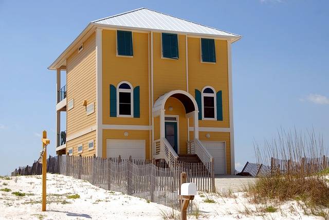 a yellow house on the beach with green shutters